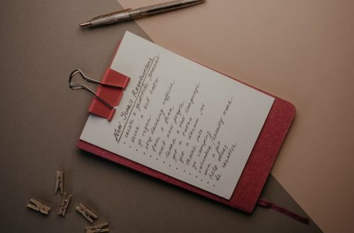 Top view of notebook with handwritten New Year's resolutions, pen, and clips on a desk.