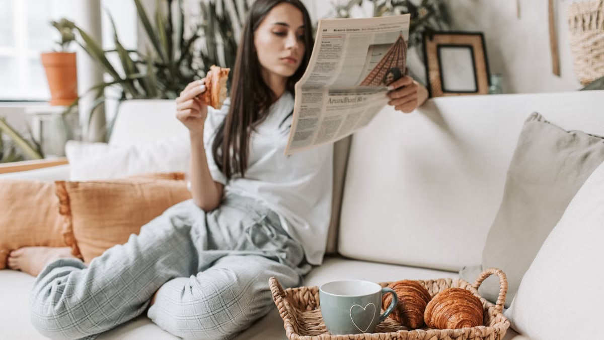 Relaxing morning scene with a woman enjoying coffee and a newspaper on a cozy couch.